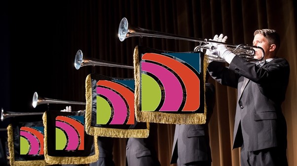 Brass players with flags hanging from their instruments, and a Campus logo displayed on the flags.
